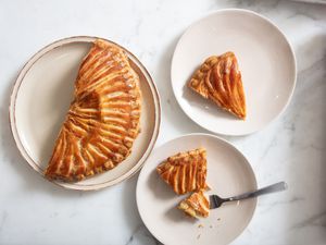 2 plates of Galette des Roi, one with a fork full of cake. A third plate with the remaining galette on it