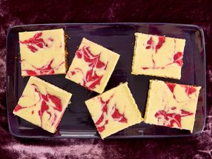 Strawberry cheesecake bars in a purple tray, on purple velvet