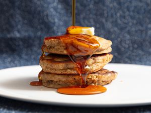 stack of banana bread pancakes with butter on top and syrup pouring over them on a white plate