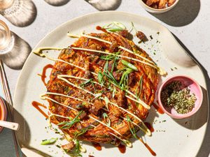 A plated carrot okonomiyaki topped with garnishes and sauces, viewed from above