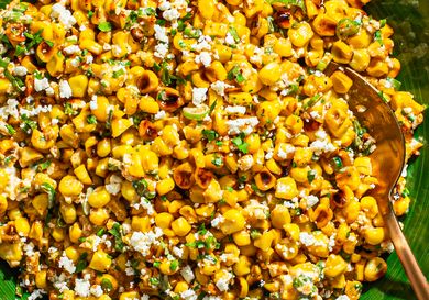 Esquites Mexican street corn salad with cheese and garnish, served in a green dish with a spoon