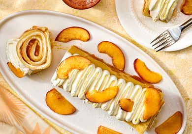 Plated dessert with rolled crepes sliced peaches and cream topping