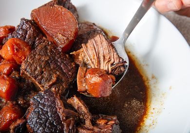 Spoon lifting beef chunks and vegetables from a bowl of stew